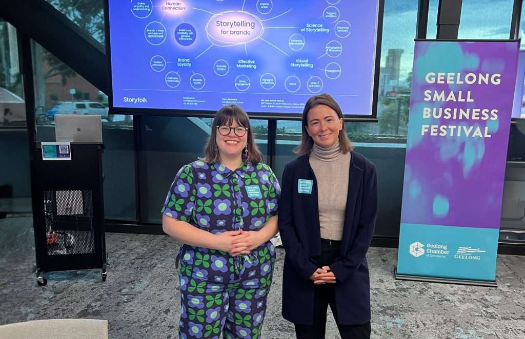 Sarah and Cass stand in front of a projector screen and banner for the Geelong Small business festival workshop they hosted called 'Storytelling for brands'